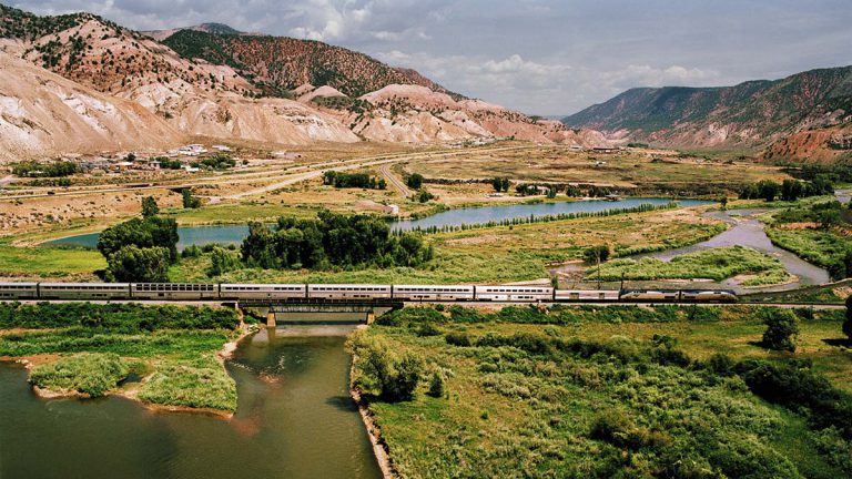 Amtrak train traveling over a bridge through a lush green valley in Utah.