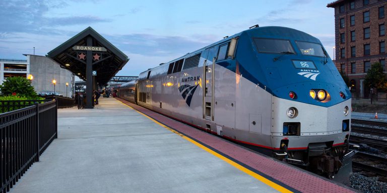 Silver and blue Amtrak train waiting for passengers at a concrete platform in Roanoke Virginia.