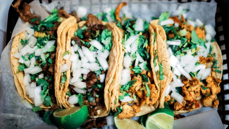 Four street tacos with chicken, onions, cilantro, and slices of lime.