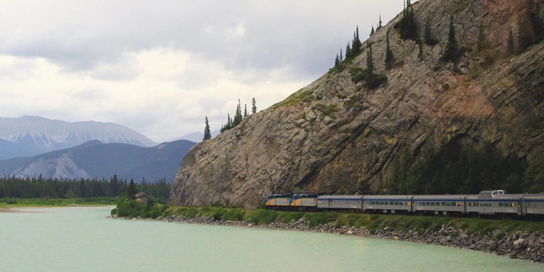 Train traveling along a river through the mountains.