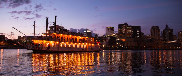 Evening riverboat cruise with lights reflecting on the water.