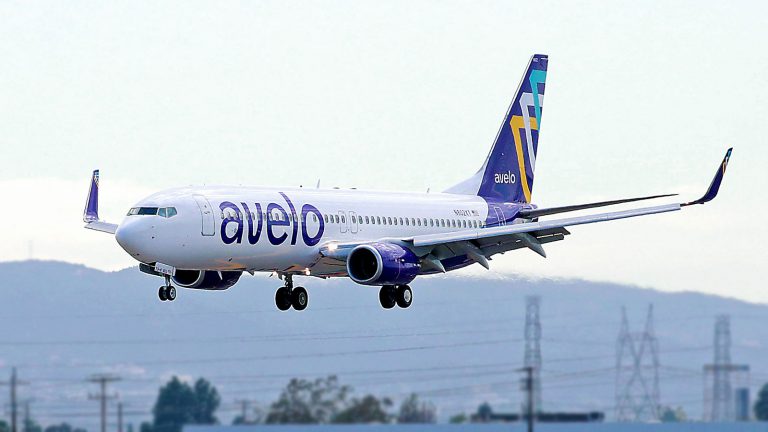 White plane with purple accents landing at airport.