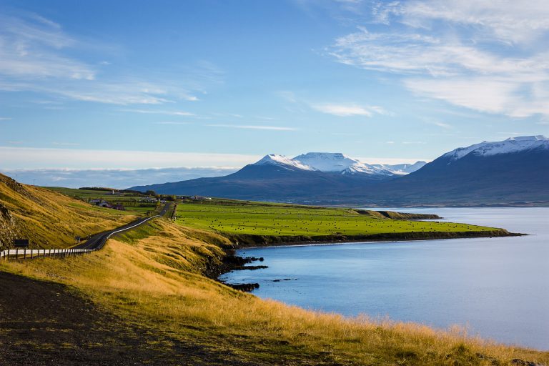 Open field and mountains wrapped by body of water.