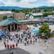 Amtrak train with train station in foreground and a large crowd standing in front of the train station.