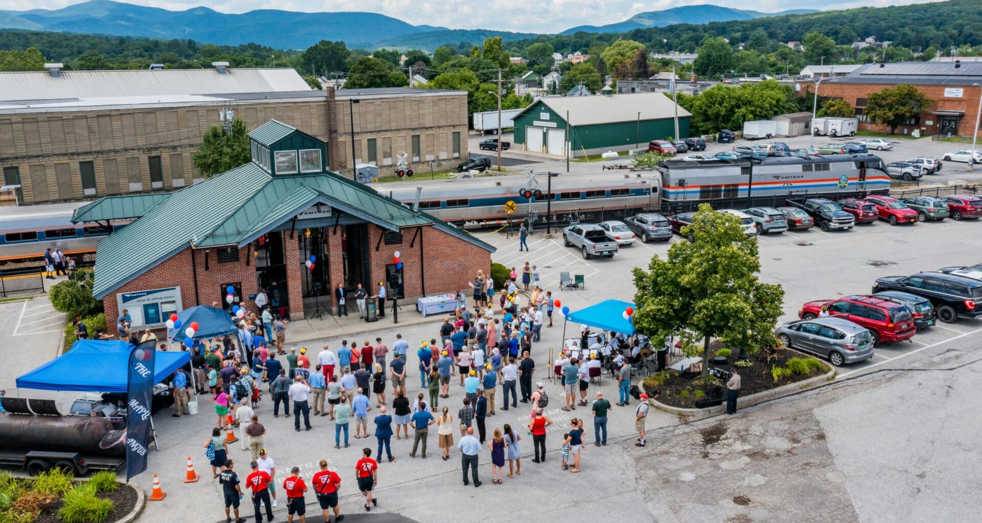 Amtrak train with train station in foreground and a large crowd standing in front of the train station.