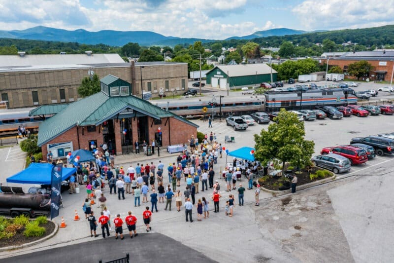 Amtrak train with train station in foreground and a large crowd standing in front of the train station.