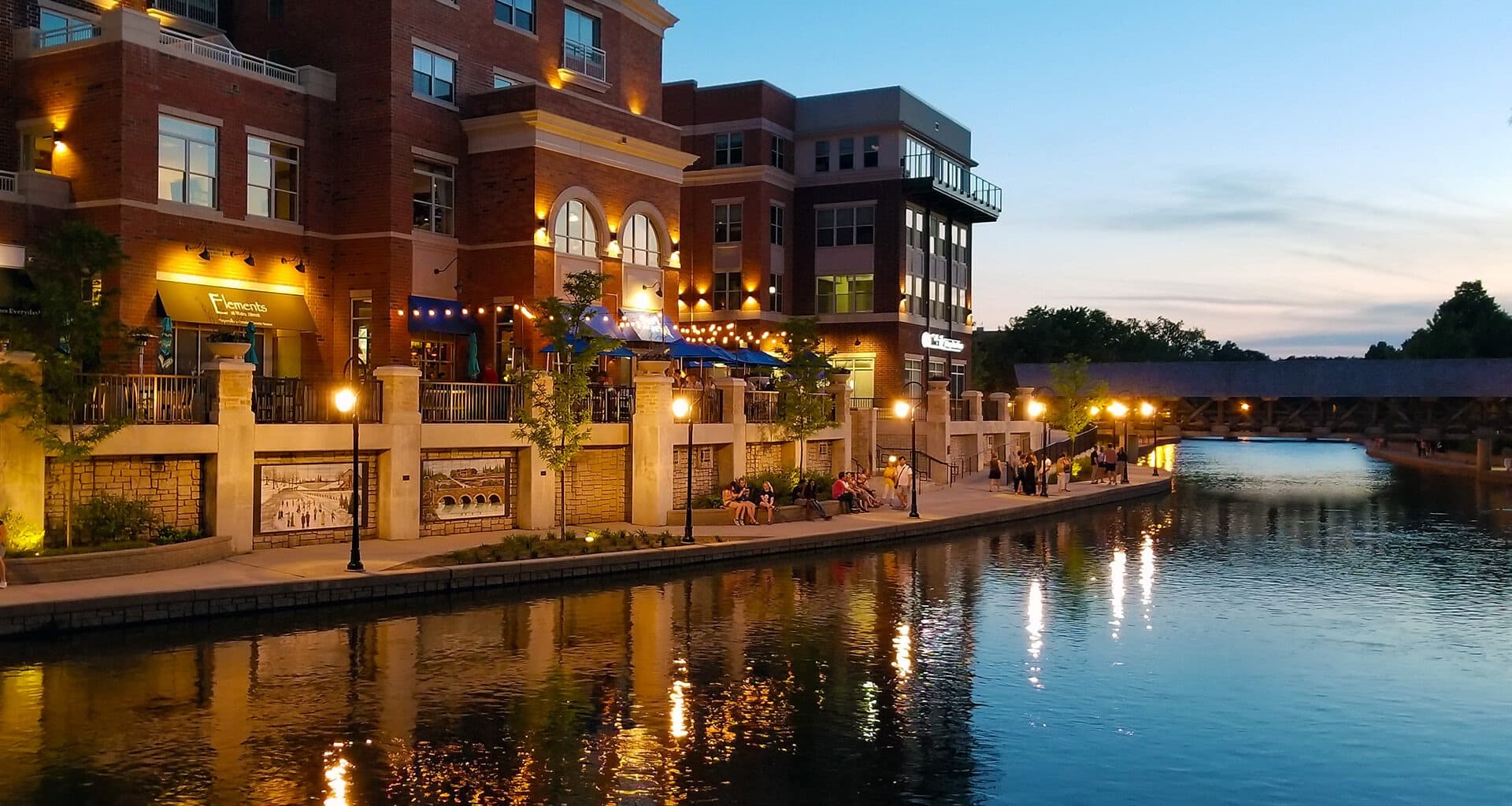 Multi-story residential building reflecting on the riverwalk next to the building during the sunset.