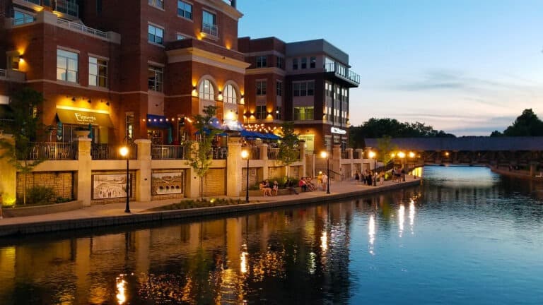 Multi-story residential building reflecting on the riverwalk next to the building during the sunset.