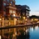 Multi-story residential building reflecting on the riverwalk next to the building during the sunset.