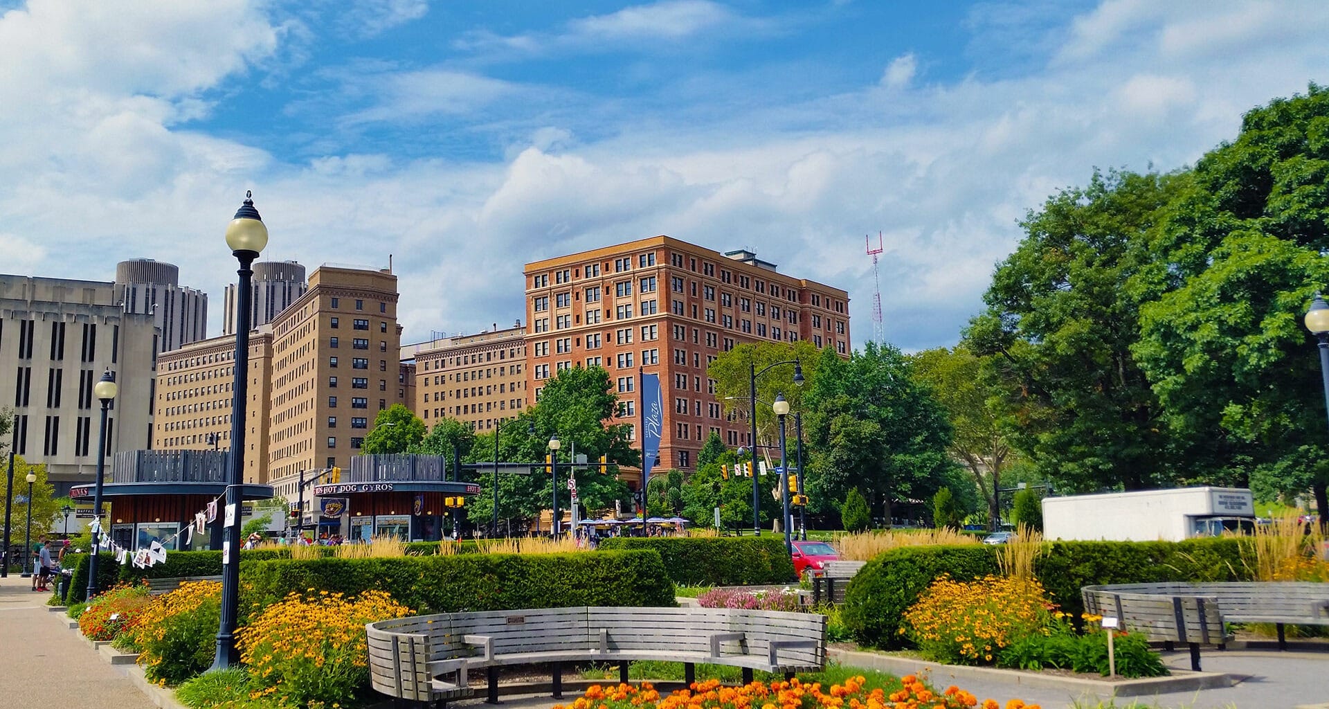 Park setting with colorful flowers and trees against taller historic buildings of red and grey.