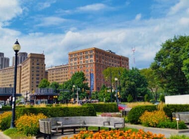 Park setting with colorful flowers and trees against taller historic buildings of red and grey.