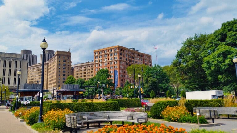 Park setting with colorful flowers and trees against taller historic buildings of red and grey.