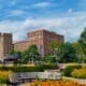 Park setting with colorful flowers and trees against taller historic buildings of red and grey.